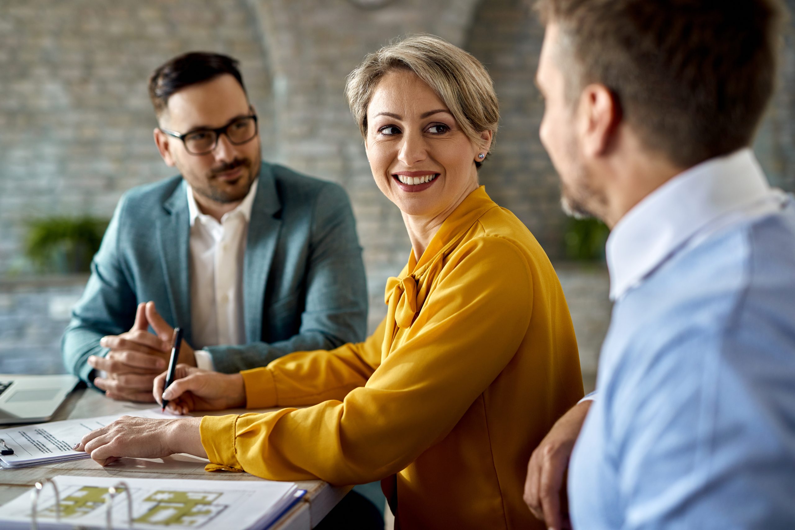 Happy couple signing paperwork on a meeting with insurance agent Happy woman signing a contract while being with her husband on a meeting with real estate agent.
